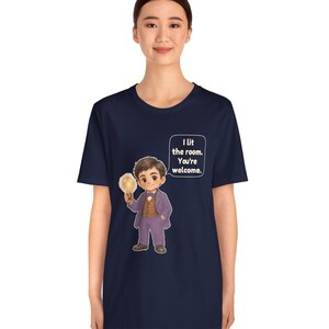 Może przedstawiać: Granatowy t-shirt z kr&oacute;tkim rękawem z grafiką postaci z kresk&oacute;wki w fioletowym garniturze, trzymającej świecącą żar&oacute;wkę. Dymek obok postaci zawiera tekst: I lit the room. You're welcome.
