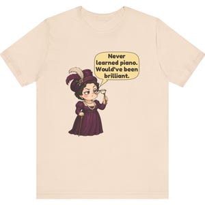 May include: A light beige t-shirt featuring a cartoon illustration of a person in a dark purple dress and hat, holding a monocle. A speech bubble contains the text: Never learned piano. Would've been brilliant.