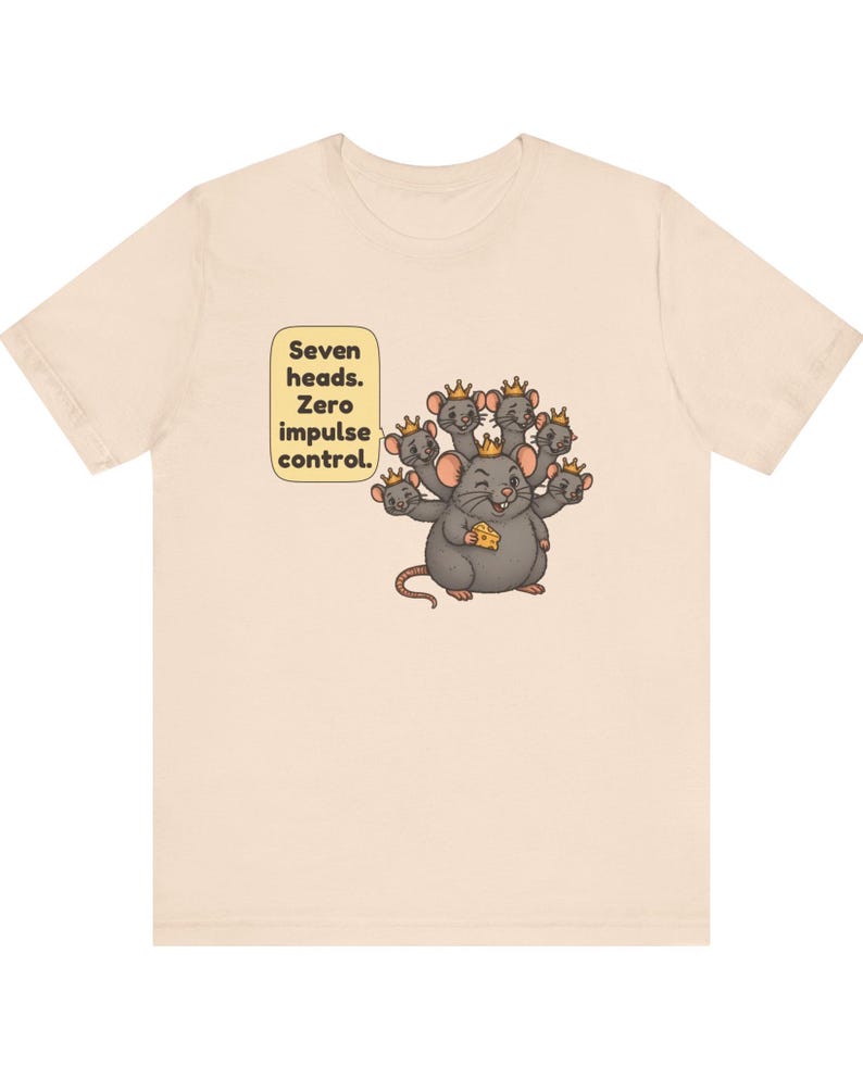 May include: A light beige t-shirt featuring a graphic of a gray seven-headed mouse wearing small gold crowns. The mouse holds a piece of yellow cheese. A speech bubble next to the mouse contains the text: Seven heads. Zero impulse control.