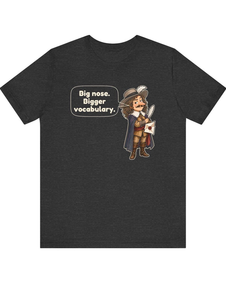 May include: A dark heather gray t-shirt featuring a cartoon illustration of a historical figure with a large nose, wearing a hat and cape, holding a quill and letter. A speech bubble contains the text: Big nose. Bigger vocabulary.