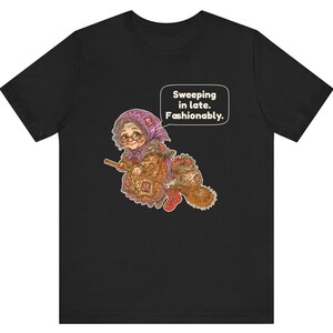 Puede incluir: Una camiseta negra con el gr&aacute;fico de una persona mayor con pa&ntilde;uelo morado y gafas montada en una escoba. La persona lleva un vestido estampado y botas rojas. Un bocadillo de texto contiene: Sweeping in late. Fashionably.