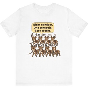 K&ouml;nnte beinhalten: Ein wei&szlig;es T-Shirt mit einer Grafik von acht braunen Rentieren in zwei Reihen, die Geschirre tragen und mit einem Seil verbunden sind. Dar&uuml;ber befindet sich eine hellgelbe Sprechblase mit dem Text: Eight reindeer. One schedule. Zero breaks.