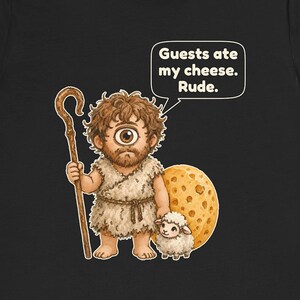 May include: A black t-shirt featuring a cartoon cyclops holding a wooden staff and standing next to a small sheep and a large wheel of Swiss cheese. A speech bubble above the cyclops contains the text: Guests ate my cheese. Rude.