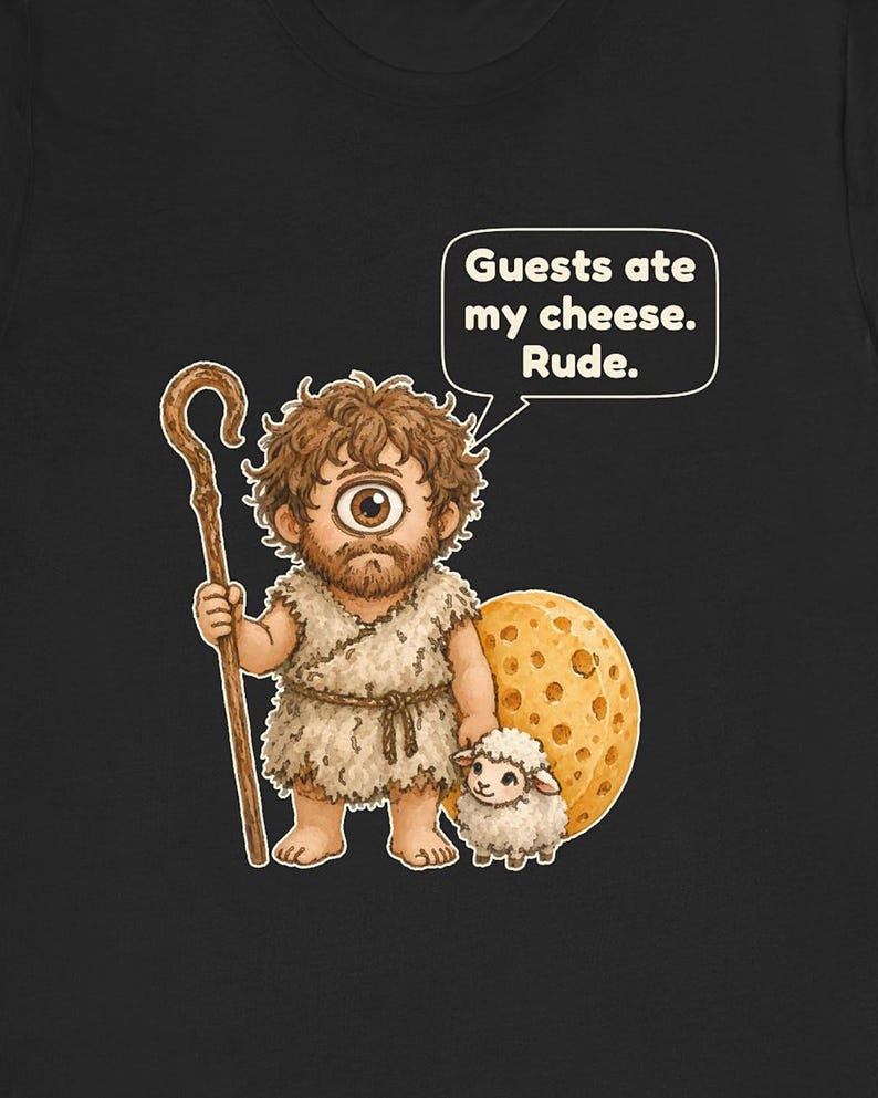 May include: A black t-shirt featuring a cartoon cyclops holding a wooden staff and standing next to a small sheep and a large wheel of Swiss cheese. A speech bubble above the cyclops contains the text: Guests ate my cheese. Rude.