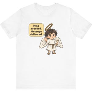 May include: A white t-shirt featuring a graphic of a cartoon angel with dark hair, white wings, and a crooked halo. The angel holds a scroll and waves, with a speech bubble containing the text: Halo crooked. Message delivered.