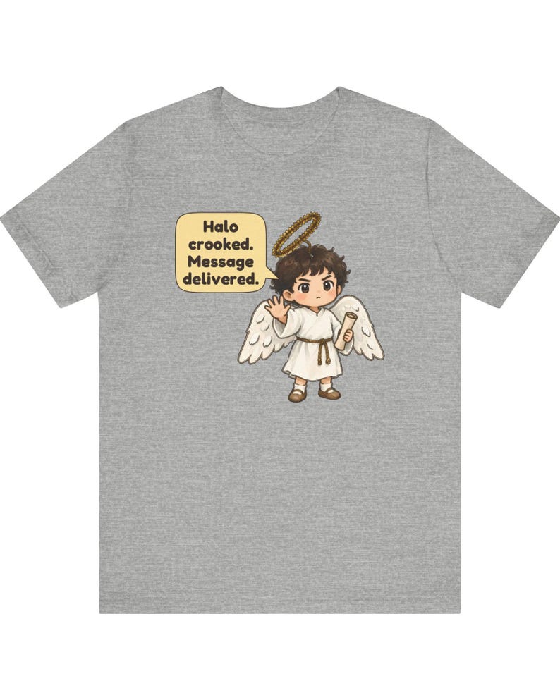 May include: A heather gray t-shirt featuring a cartoon angel with brown hair, white wings, and a crooked halo. The angel wears a white robe with a brown belt and holds a scroll. A speech bubble contains the text: Halo crooked. Message delivered.
