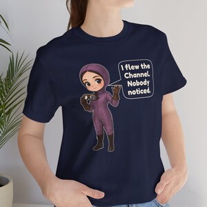 Puede incluir: Una camiseta azul marino con una ilustraci&oacute;n de dibujos animados de un piloto con traje de vuelo morado sosteniendo unas gafas. Un globo de texto contiene: I flew the Channel. Nobody noticed. El dise&ntilde;o est&aacute; centrado en el pecho.