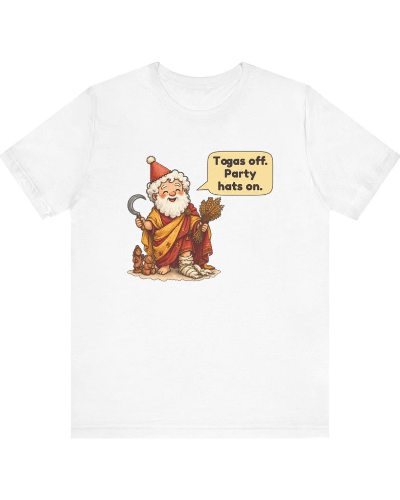 May include: A white t-shirt featuring a cartoon illustration of a bearded figure wearing a red and yellow robe, a red party hat, and a bandage on one foot. The figure holds a sickle and wheat, with a speech bubble that reads: Togas off. Party hats on.
