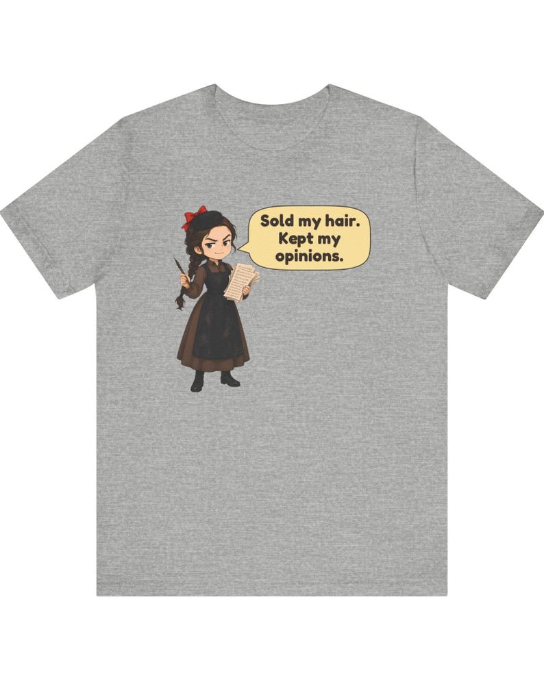 May include: A heather gray t-shirt featuring a cartoon illustration of a character with dark hair, a red bow, and a brown dress with a black apron. The character holds a pen and papers, with a speech bubble that reads: Sold my hair. Kept my opinions.