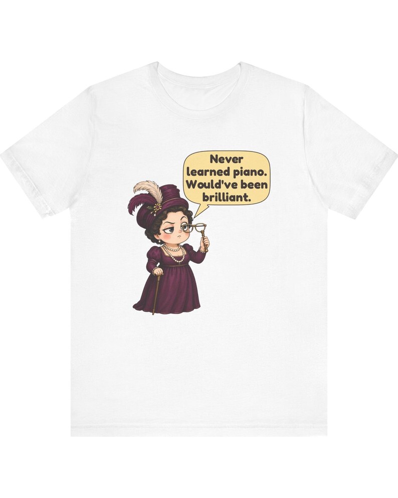 May include: A white t-shirt featuring a cartoon illustration of a person in a dark purple dress, hat with feathers, and pearls, holding a monocle. A speech bubble contains the text: Never learned piano. Would've been brilliant.