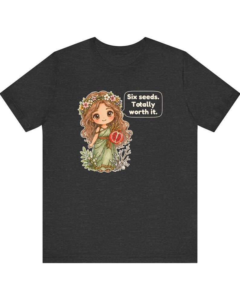May include: A dark gray t-shirt featuring a graphic of a cartoon character with long brown hair, a flower crown, and a green dress holding a pomegranate. A speech bubble next to the character contains the text: Six seeds. Totally worth it.