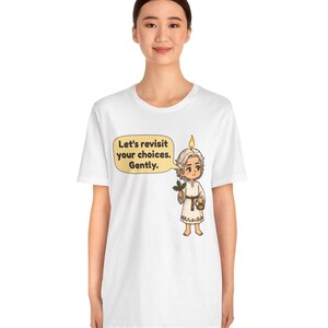 May include: A white t-shirt featuring a cartoon character with a candle flame on their head, holding a sprig of holly and a small basket. A speech bubble next to the character contains the text: Let's revisit your choices. Gently.
