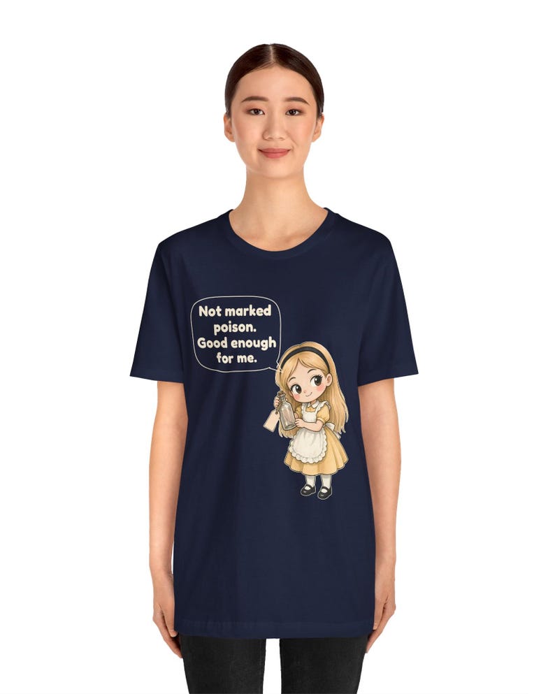 May include: A navy blue t-shirt featuring a graphic of a blonde character in a yellow dress and white apron holding a glass bottle. A speech bubble above the character contains the text: Not marked poison. Good enough for me.
