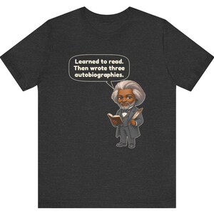 Puede incluir: Una camiseta gris jaspeado oscuro con una ilustraci&oacute;n de estilo caricatura de Frederick Douglass sosteniendo un libro y una pluma. Un globo de texto sobre la figura contiene el texto: Learned to read. Then wrote three autobiographies.