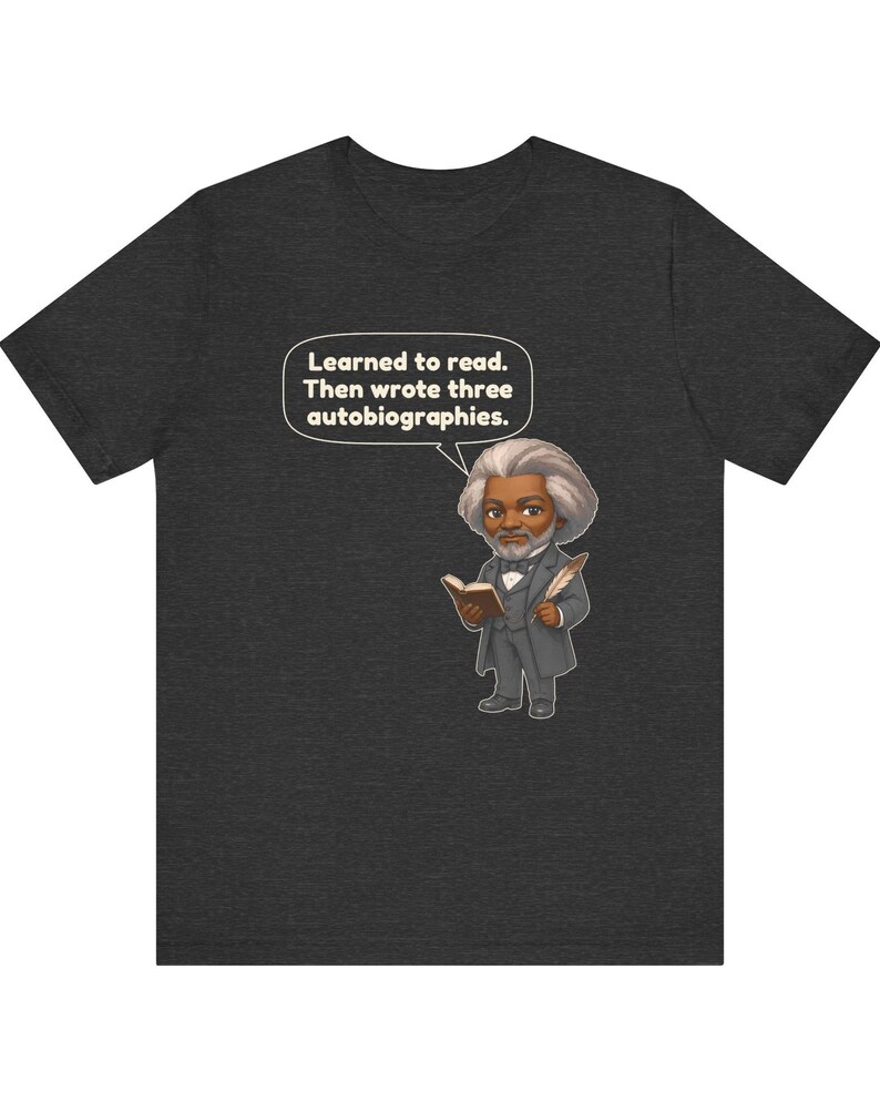Puede incluir: Una camiseta gris jaspeado oscuro con una ilustraci&oacute;n de estilo caricatura de Frederick Douglass sosteniendo un libro y una pluma. Un globo de texto sobre la figura contiene el texto: Learned to read. Then wrote three autobiographies.