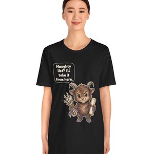Puede incluir: Una camiseta negra con el gr&aacute;fico de una criatura marr&oacute;n con cuernos que sostiene un manojo de palos y un pergamino. Un globo de texto sobre la criatura contiene el texto: Naughty list? I'll take it from here.