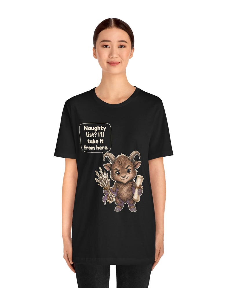 Puede incluir: Una camiseta negra con el gr&aacute;fico de una criatura marr&oacute;n con cuernos que sostiene un manojo de palos y un pergamino. Un globo de texto sobre la criatura contiene el texto: Naughty list? I'll take it from here.