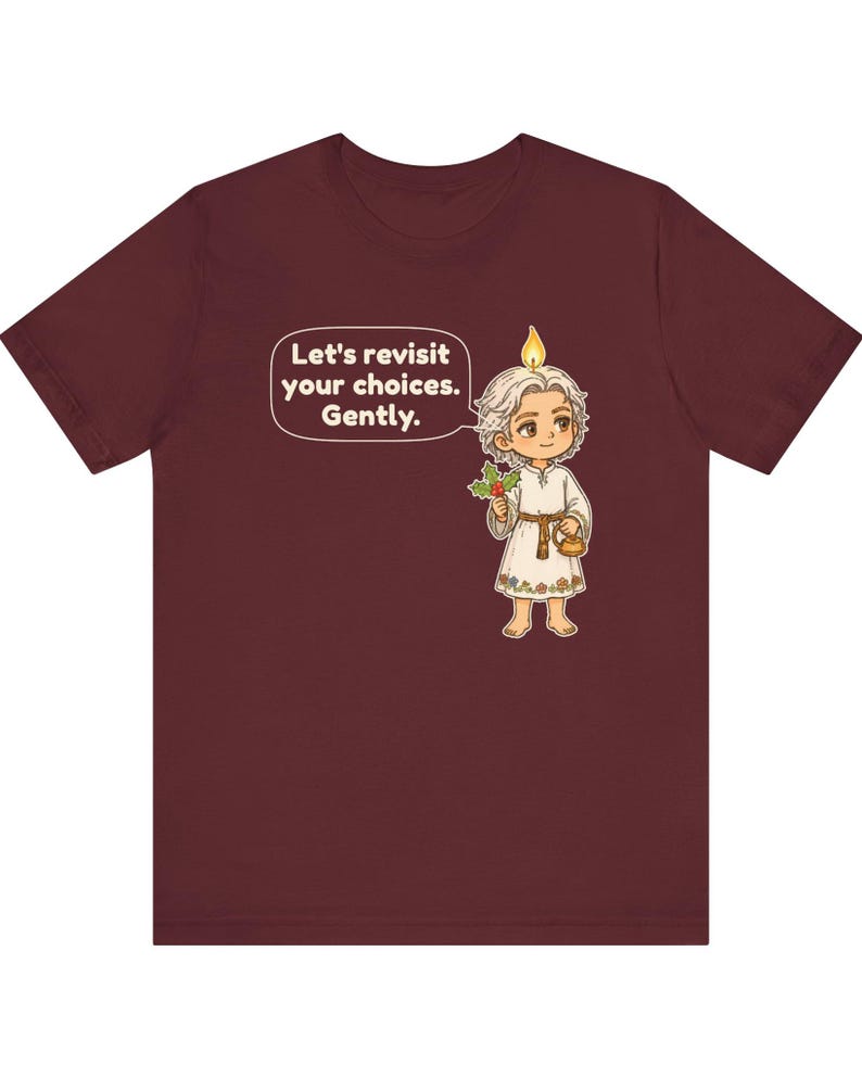 May include: A maroon t-shirt featuring a cartoon character with a candle flame on their head, holding a sprig of holly and a small gold pot. A speech bubble contains the text: Let's revisit your choices. Gently. The character wears a white tunic.