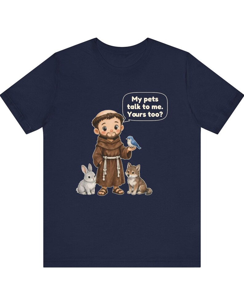 May include: A navy blue t-shirt featuring a cartoon illustration of a monk in a brown robe with a white rope belt. The monk is surrounded by a gray rabbit, a brown wolf, and a blue bird. A speech bubble contains the text: My pets talk to me. Yours too?