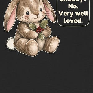 May include: A brown plush bunny with a white tail and pink inner ears holds a sprig of holly with red berries. A speech bubble next to the bunny contains the text: Shabby? No. Very well loved. The illustration is set against a dark background.