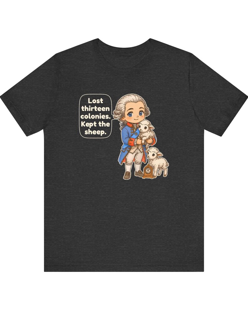 Peut inclure: Un t-shirt gris anthracite chin&eacute; avec une illustration de style dessin anim&eacute; repr&eacute;sentant un personnage historique en manteau bleu tenant un agneau, accompagn&eacute; d'un autre agneau et d'une petite horloge. Une bulle contient le texte : Lost thirteen colonies. Kept the sheep.