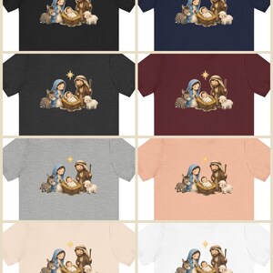 May include: A collection of eight short-sleeve t-shirts in various colors, each featuring a central graphic illustration of a nativity scene with a baby in a manger, a person in a blue head covering, a person with a staff, a donkey, a sheep, and a star.