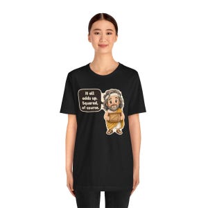 Pu&ograve; includere: Una t-shirt nera a maniche corte con un'illustrazione a cartoni animati di un uomo barbuto in toga che tiene in mano un triangolo rettangolo incorniciato. Un fumetto contiene il testo: It all adds up. Squared, of course.