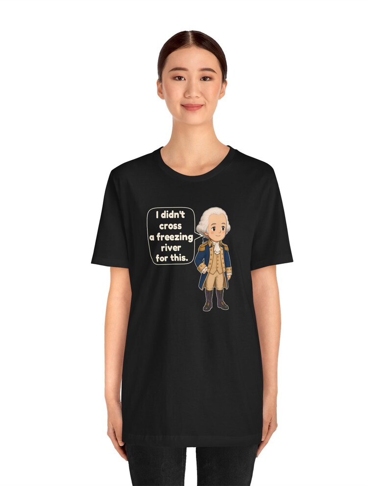 May include: A black t-shirt featuring a cartoon illustration of a historical figure in a blue and tan uniform. A speech bubble next to the character contains the white text: I didn't cross a freezing river for this.