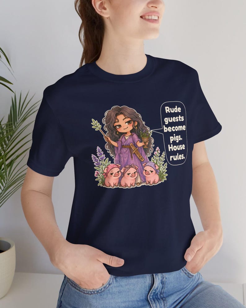 May include: A navy blue t-shirt featuring a graphic illustration of a long-haired character in a purple robe holding a wand and a goblet, surrounded by three small pigs. The text reads: Rude guests become pigs. House rules.