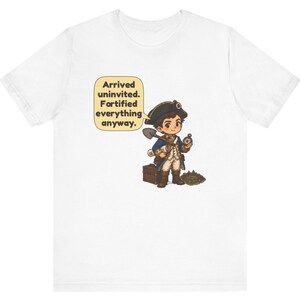 May include: A white t-shirt featuring a cartoon illustration of a historical explorer in a blue coat and tricorn hat, holding a shovel and compass. A speech bubble contains the text: Arrived uninvited. Fortified everything anyway.