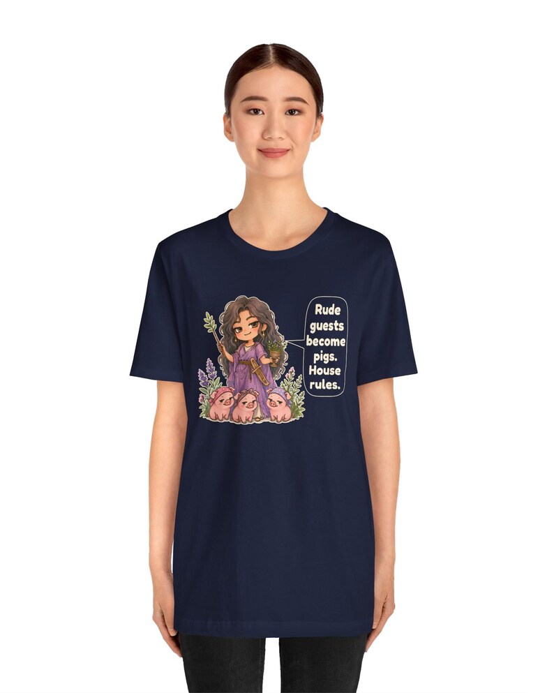 May include: A navy blue t-shirt featuring a graphic of a character with long dark hair in a purple dress holding a staff and a potted plant, surrounded by three small pigs. The text reads: Rude guests become pigs. House rules.