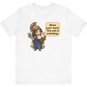 Puede incluir: Una camiseta blanca con el gr&aacute;fico de un personaje con casco dorado y t&uacute;nica azul, sosteniendo una rama de olivo y un portapapeles. Un b&uacute;ho est&aacute; sobre el hombro junto a un globo de texto que dice, Show your work. The owl is watching.