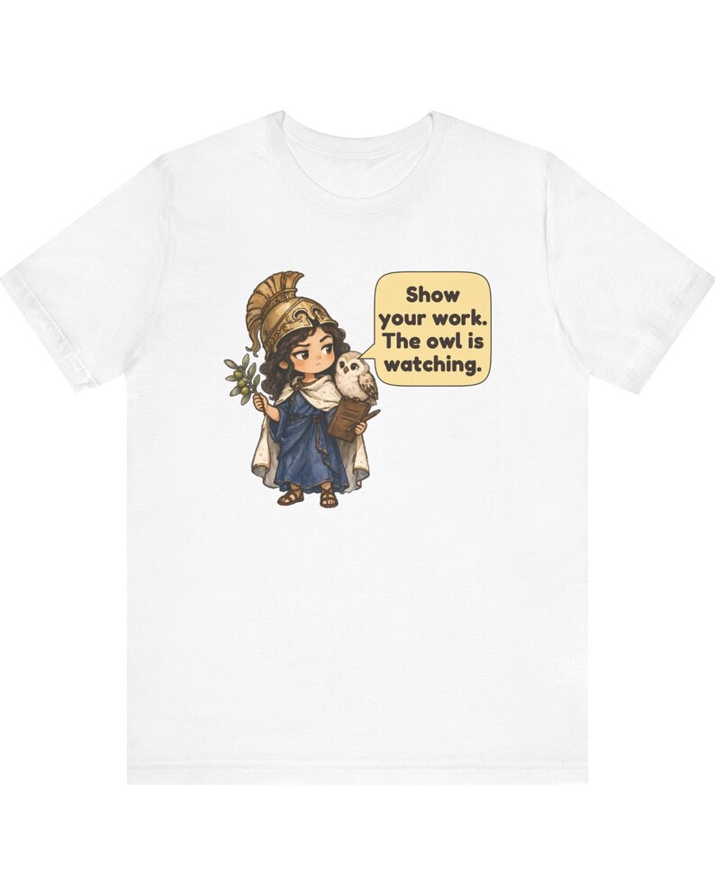 Puede incluir: Una camiseta blanca con el gr&aacute;fico de un personaje con casco dorado y t&uacute;nica azul, sosteniendo una rama de olivo y un portapapeles. Un b&uacute;ho est&aacute; sobre el hombro junto a un globo de texto que dice, Show your work. The owl is watching.
