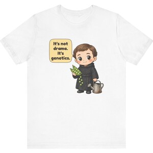 May include: A white t-shirt featuring a cartoon illustration of a monk holding a pea pod and a small watering can. A speech bubble next to the character contains the text: It's not drama. It's genetics. The design is centered on the chest.