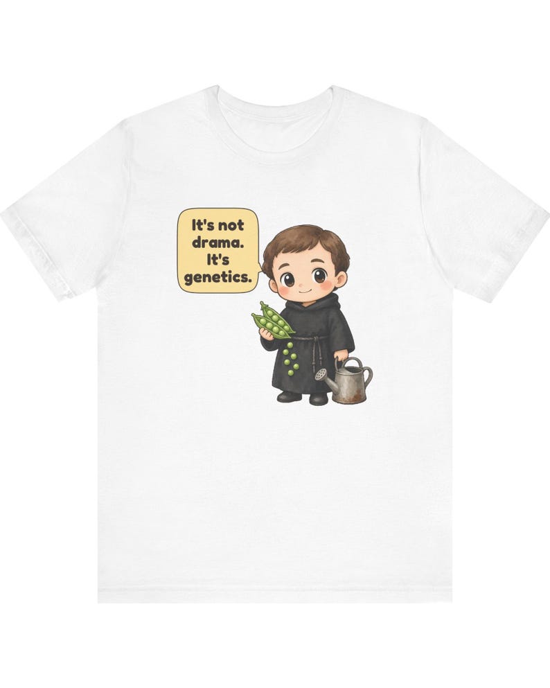 May include: A white t-shirt featuring a cartoon illustration of a monk holding a pea pod and a small watering can. A speech bubble next to the character contains the text: It's not drama. It's genetics. The design is centered on the chest.