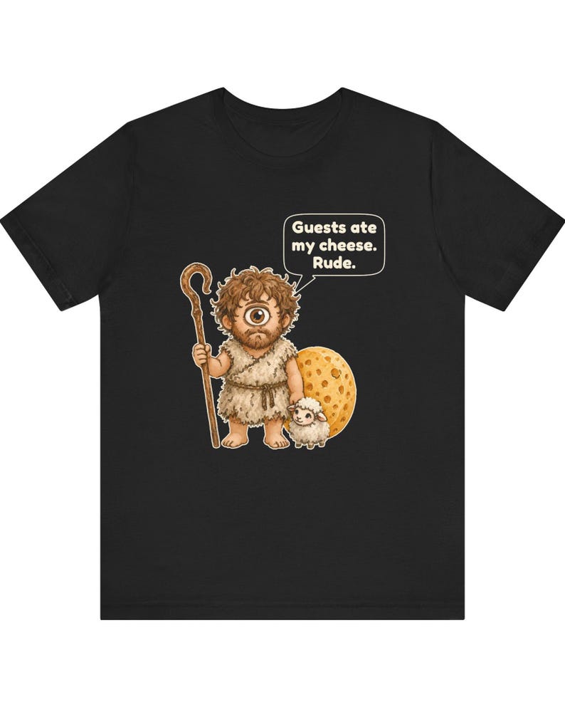 May include: A black t-shirt featuring a graphic of a one-eyed cyclops holding a wooden staff next to a small white sheep and a large wheel of Swiss cheese. A speech bubble above the cyclops contains the text: Guests ate my cheese. Rude.
