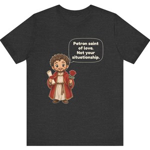 Puede incluir: Una camiseta gris oscuro de manga corta con una figura de dibujos animados con t&uacute;nica roja que sostiene un pergamino y una rosa roja. Un globo de texto contiene: Patron saint of love. Not your situationship.