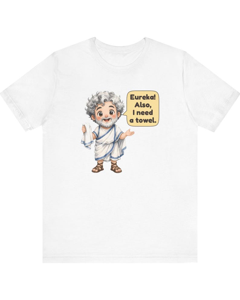 May include: A white short-sleeve t-shirt featuring a cartoon illustration of a bearded man in a white toga and brown sandals holding a white towel. A yellow speech bubble next to the character contains the text: Eureka! Also, I need a towel.