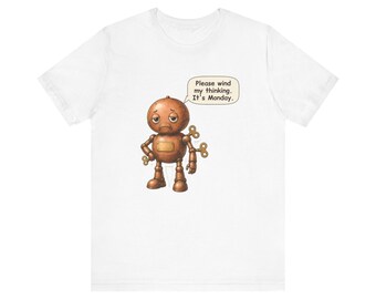May include: A white t-shirt featuring a graphic of a round, copper-colored robot with a sad expression. The robot has wind-up keys on its back and side. A speech bubble above the robot contains the text: Please wind my thinking. It's Monday.