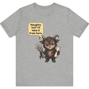 Puede incluir: Una camiseta gris jaspeado con el gr&aacute;fico de una peque&ntilde;a criatura marr&oacute;n con cuernos que sostiene un manojo de palos y un pergamino. Un globo de texto amarillo sobre la criatura contiene el texto: Naughty list? I'll take it from here.
