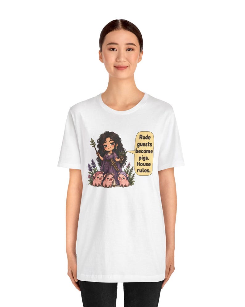May include: A white t-shirt featuring a graphic of a dark-haired character in a purple dress holding a staff and a small pot, surrounded by three small pigs. A speech bubble contains the text: Rude guests become pigs. House rules.