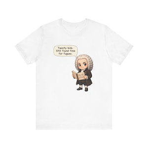 May include: A white short-sleeve t-shirt featuring a cartoon illustration of a historical figure with a powdered wig holding a music book. A speech bubble above the character contains the text: Twenty kids. Still found time for fugues.