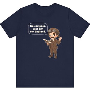 May include: A navy blue t-shirt featuring a cartoon illustration of a pilot with a mustache, wearing a brown suit and aviator goggles, holding a small airplane. A speech bubble contains the text: No compass. Just aim for England.