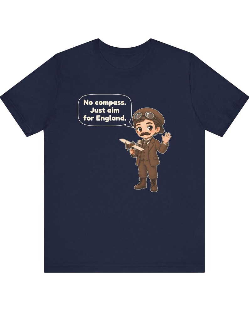 May include: A navy blue t-shirt featuring a cartoon illustration of a pilot with a mustache, wearing a brown suit and aviator goggles, holding a small airplane. A speech bubble contains the text: No compass. Just aim for England.