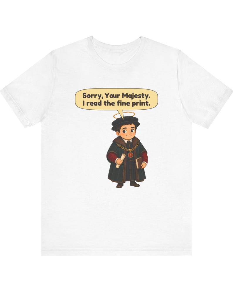 May include: A white t-shirt featuring a cartoon illustration of a person wearing a black robe, a gold chain, and a halo. The character holds a scroll and a book. A speech bubble above the character contains the text: Sorry, Your Majesty. I read the fine print.