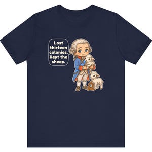 Peut inclure: Un t-shirt bleu marine avec une illustration de style dessin anim&eacute; repr&eacute;sentant une personne en tenue du XVIIIe si&egrave;cle tenant un agneau, avec un autre agneau et une petite horloge. Une bulle contient le texte : Lost thirteen colonies. Kept the sheep.