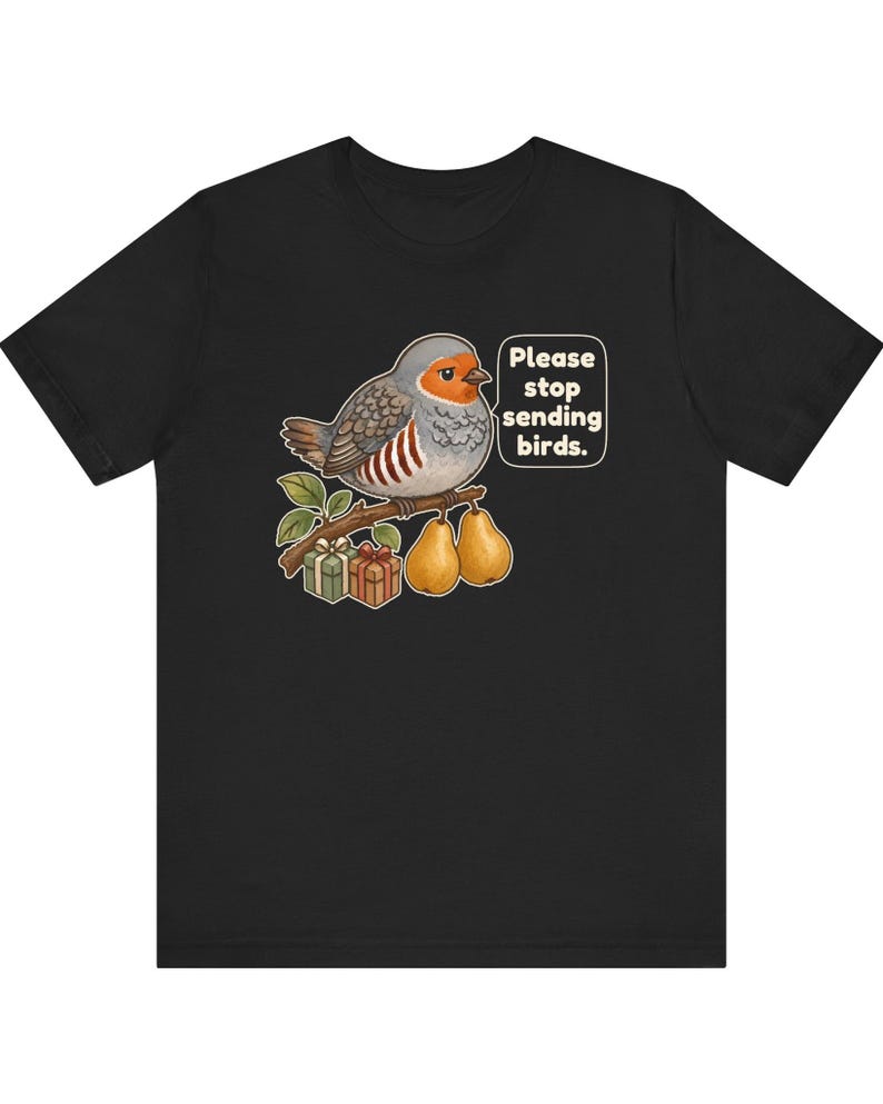 K&ouml;nnte beinhalten: Ein schwarzes T-Shirt mit einer Grafik eines grauen und orangefarbenen Vogels, der auf einem Ast mit zwei Birnen und zwei kleinen Geschenkkartons sitzt. Eine Sprechblase neben dem Vogel enth&auml;lt den Text: "Please stop sending birds."