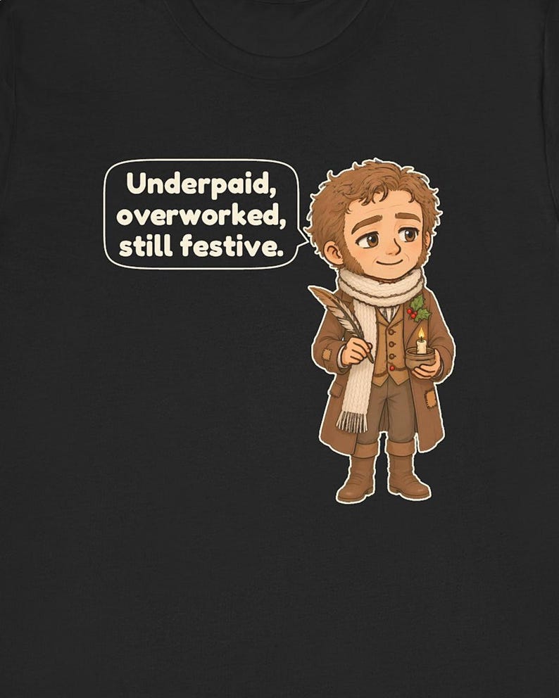 May include: A black t-shirt featuring a cartoon illustration of a person in a brown coat, white scarf, and boots, holding a quill and a candle. A speech bubble contains the text: Underpaid, overworked, still festive.