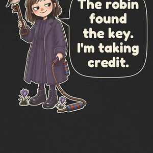 May include: A graphic illustration on a black background featuring a person in a dark purple coat holding a key with a robin perched on it. A speech bubble contains the text: The robin found the key. I'm taking credit. A rope with red and blue striped ends hangs down near purple flowers.