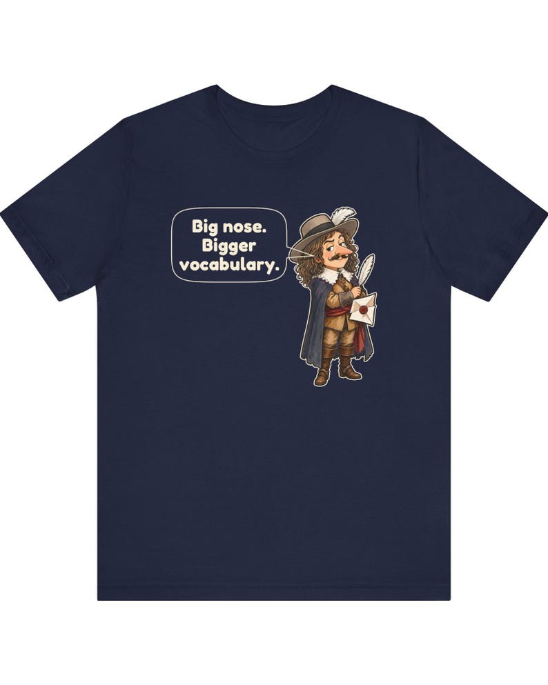 May include: A navy blue short-sleeve t-shirt featuring a cartoon illustration of a historical figure with a large nose, wearing a hat and cape, holding a quill and letter. A speech bubble contains the text: Big nose. Bigger vocabulary.